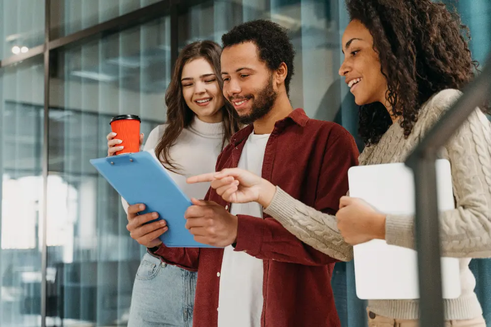 Duas mulheres e um homem analisando um documento em pé em ambiente corporativo, onde exercem suas Power Skills.