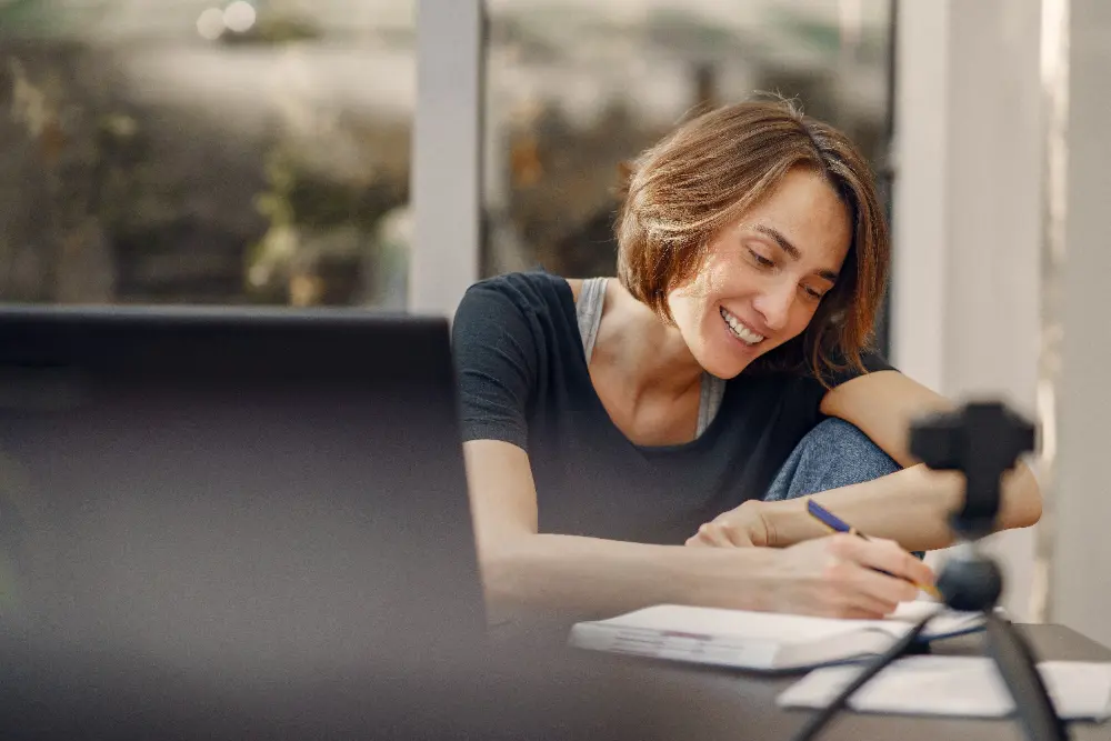 Mulher sorridente faz anotações sobre uma mesa de trabalho